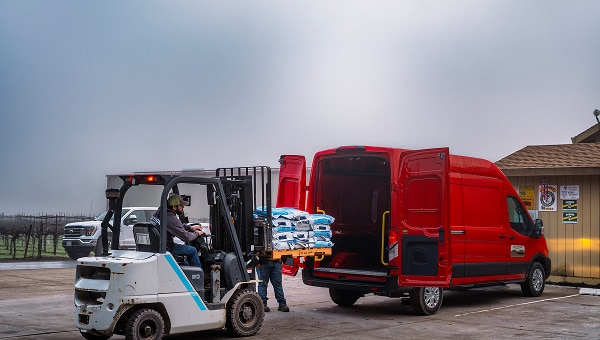 Ford E-Transit roja siendo cargada con sacos por una carretilla elevadora.